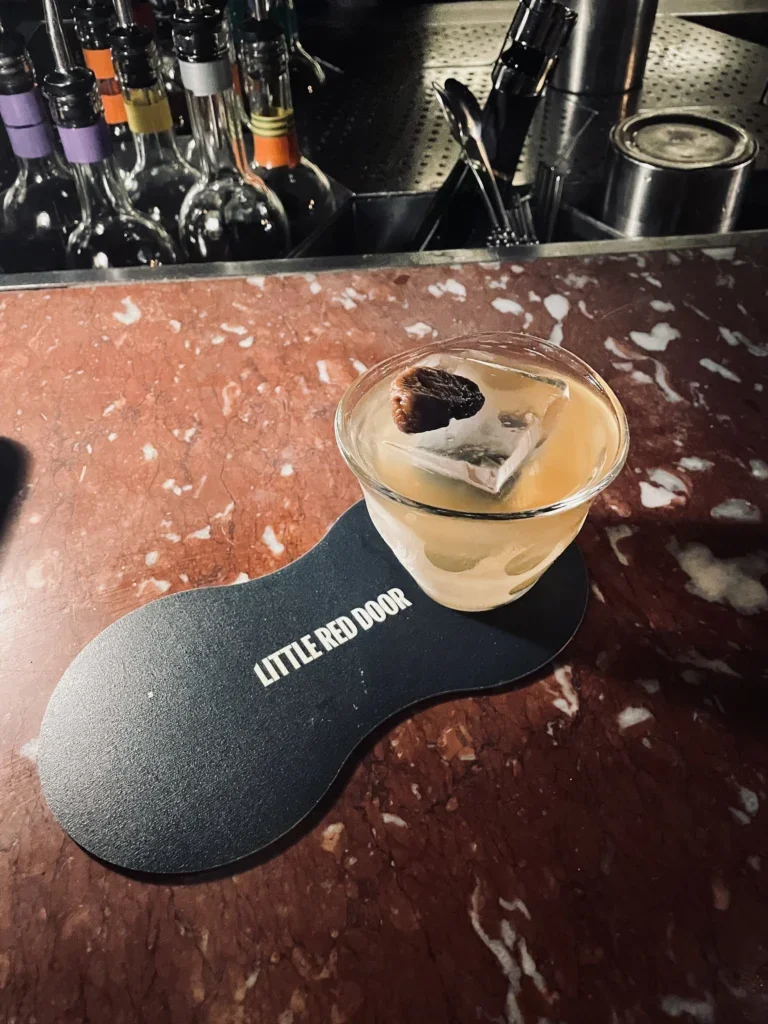 A cocktail sits on a Little Red Door bar mat