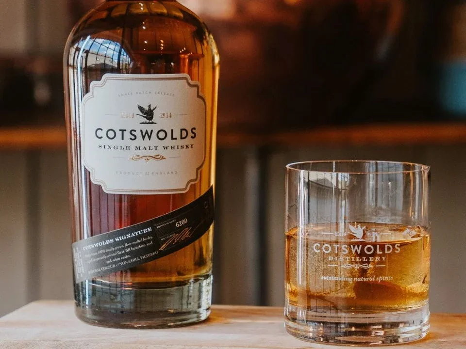 Cotswold whisky bottle next to a glass with ice